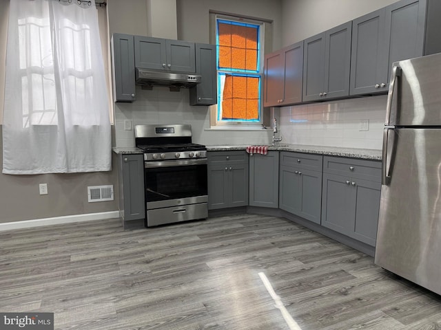 kitchen featuring light wood-type flooring, tasteful backsplash, light stone counters, gray cabinetry, and stainless steel appliances