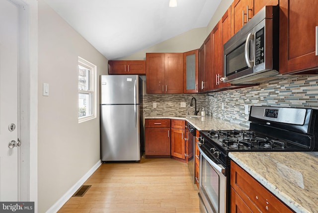 kitchen featuring lofted ceiling, glass insert cabinets, appliances with stainless steel finishes, light stone countertops, and a sink