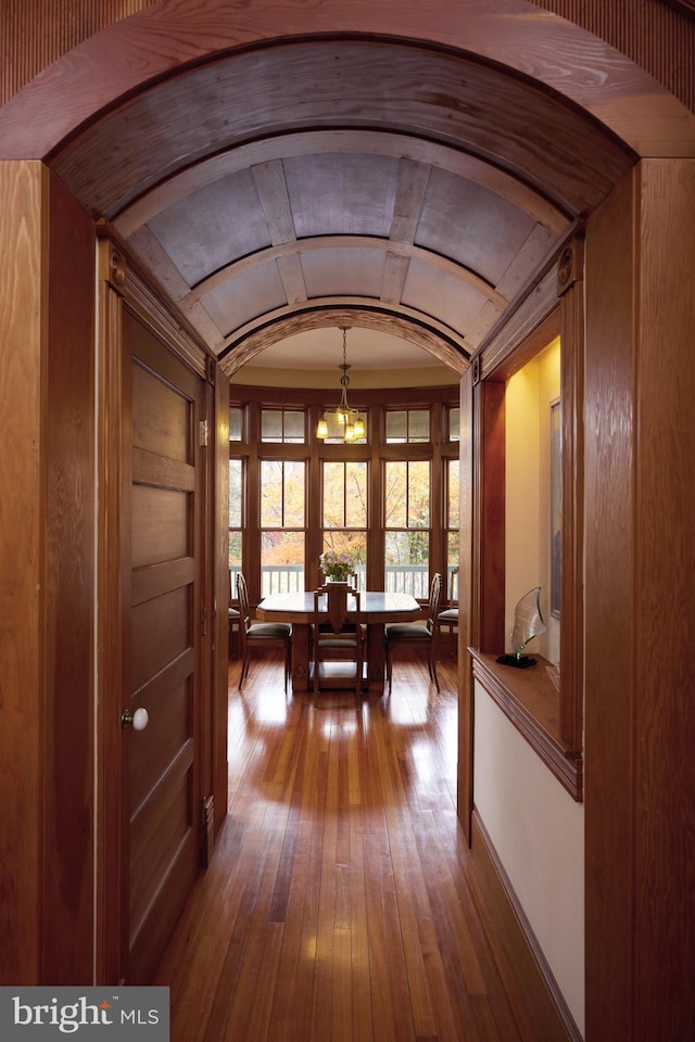 corridor with hardwood / wood-style flooring, wooden walls, and a notable chandelier