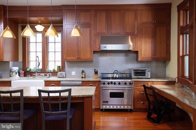 kitchen featuring a kitchen bar, appliances with stainless steel finishes, backsplash, range hood, and light stone counters