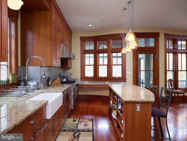 kitchen with a kitchen island, hanging light fixtures, light stone countertops, dark wood-type flooring, and wall chimney exhaust hood