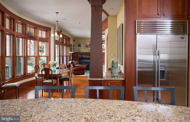 kitchen with light stone countertops, hanging light fixtures, stainless steel built in refrigerator, and light hardwood / wood-style flooring