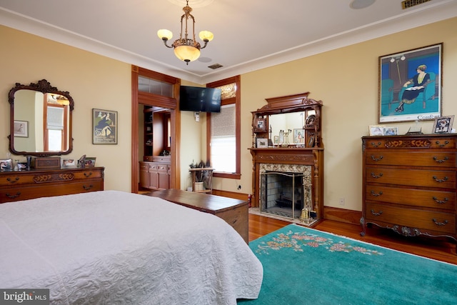 bedroom featuring a fireplace, dark hardwood / wood-style floors, ensuite bath, an inviting chandelier, and crown molding