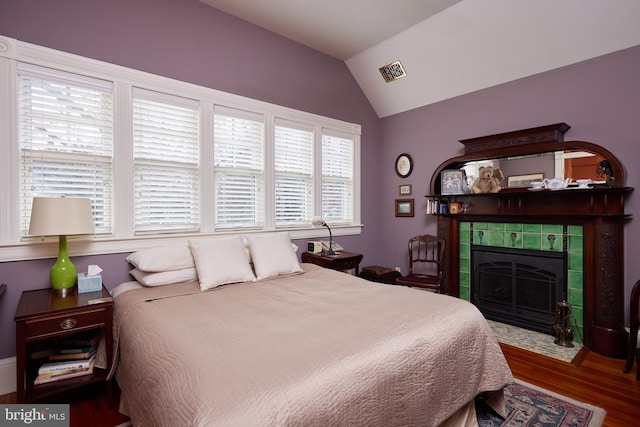 bedroom featuring wood-type flooring, vaulted ceiling, and a tile fireplace