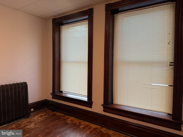 interior space with hardwood / wood-style floors, a drop ceiling, and radiator heating unit