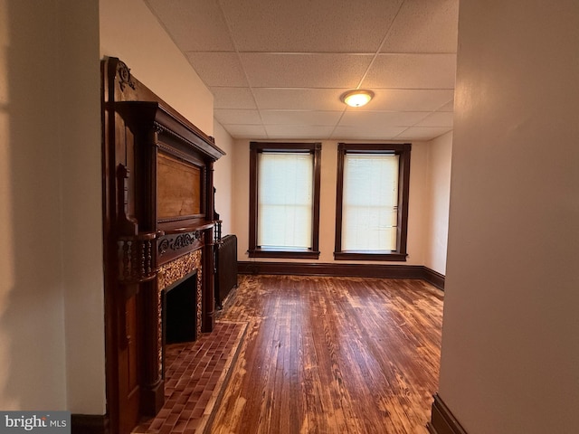 unfurnished living room with a paneled ceiling, dark hardwood / wood-style flooring, and a tile fireplace