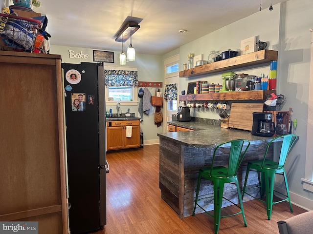 kitchen with a kitchen breakfast bar, kitchen peninsula, wood-type flooring, decorative light fixtures, and fridge