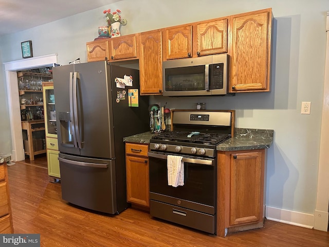 kitchen with stainless steel appliances, hardwood / wood-style flooring, and dark stone counters