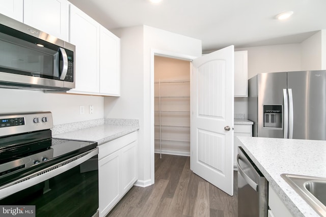 kitchen with sink, white cabinetry, light hardwood / wood-style flooring, light stone countertops, and appliances with stainless steel finishes