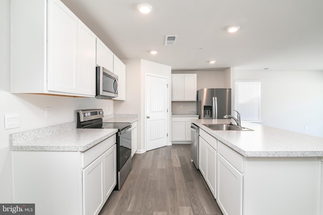 kitchen featuring appliances with stainless steel finishes, an island with sink, dark hardwood / wood-style flooring, sink, and white cabinetry