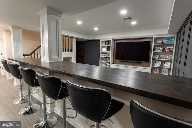 bar with wood counters, ornate columns, built in shelves, and light hardwood / wood-style flooring