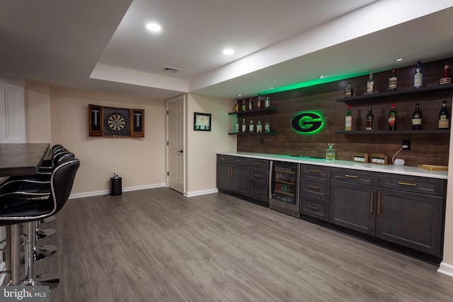 bar featuring beverage cooler, dark brown cabinets, and light hardwood / wood-style flooring