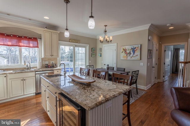 kitchen featuring stainless steel dishwasher, hanging light fixtures, an island with sink, beverage cooler, and sink