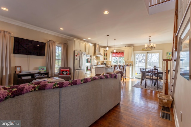 living room featuring a healthy amount of sunlight, an inviting chandelier, crown molding, and wood-type flooring