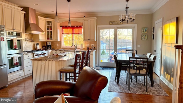 kitchen with light stone countertops, pendant lighting, wall chimney range hood, and a kitchen island