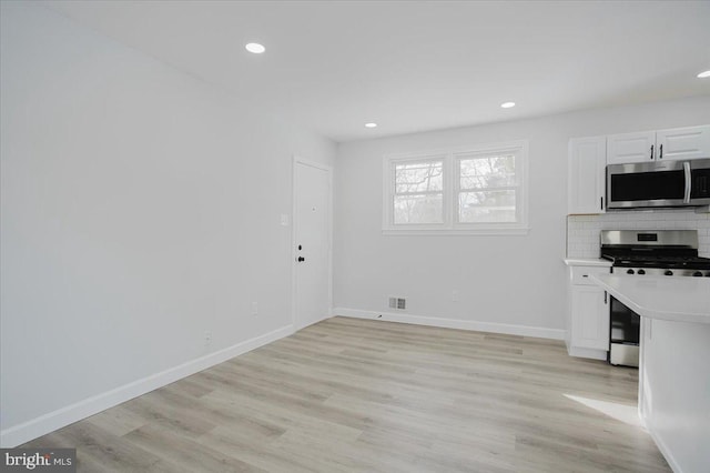 kitchen with backsplash, white cabinetry, stainless steel appliances, and light wood-type flooring