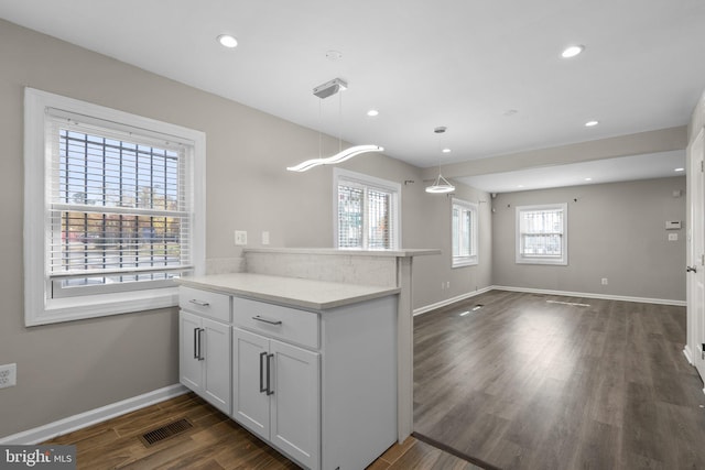 kitchen with kitchen peninsula, a healthy amount of sunlight, white cabinets, dark hardwood / wood-style floors, and hanging light fixtures