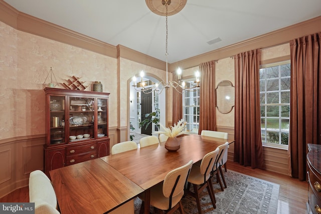 dining space with hardwood / wood-style flooring, ornamental molding, and a notable chandelier