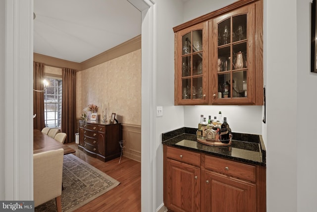 bar with dark stone countertops, hardwood / wood-style flooring, and crown molding