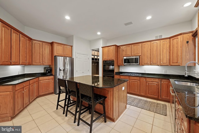 kitchen with sink, a center island, dark stone counters, and appliances with stainless steel finishes