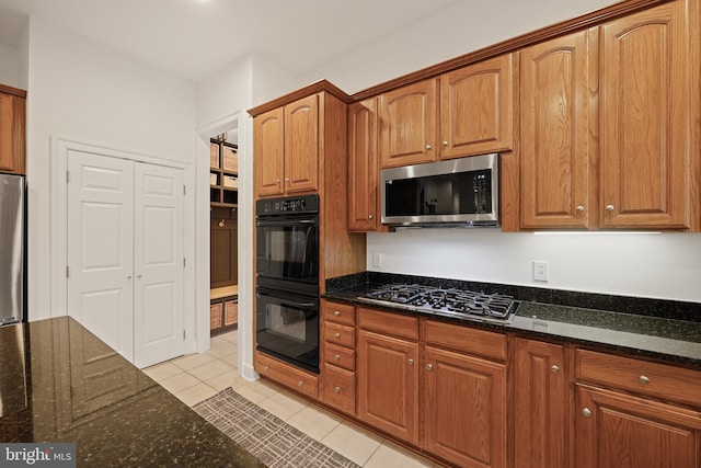 kitchen with light tile patterned floors, stainless steel appliances, and dark stone counters