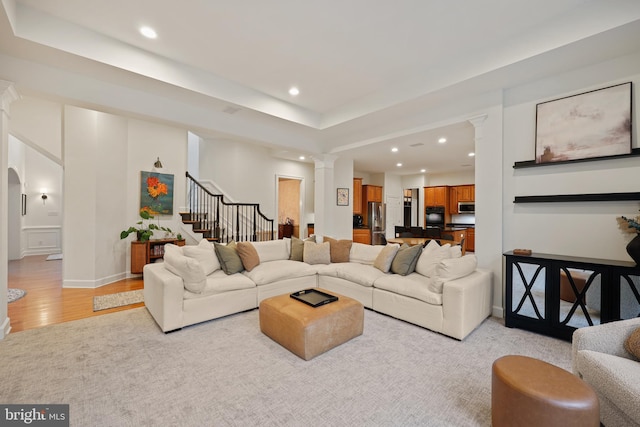 living room with decorative columns, a tray ceiling, and light hardwood / wood-style flooring