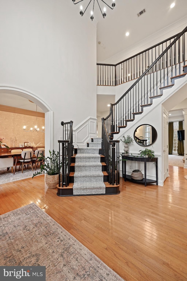 staircase featuring a notable chandelier, a towering ceiling, ornamental molding, and hardwood / wood-style floors