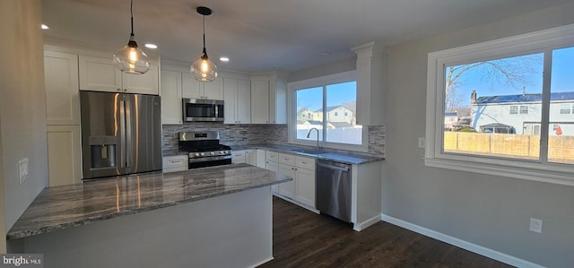 kitchen featuring sink, white cabinets, stone countertops, pendant lighting, and appliances with stainless steel finishes