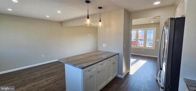 kitchen with white cabinetry, dark stone countertops, stainless steel refrigerator, hanging light fixtures, and dark wood-type flooring