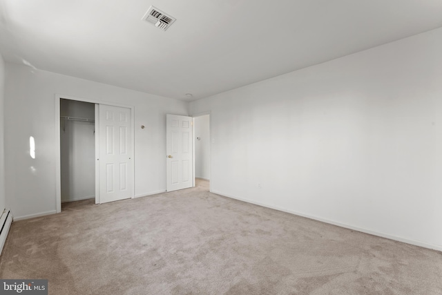 unfurnished bedroom with light colored carpet, a closet, and baseboard heating