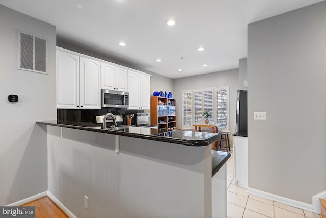 kitchen featuring kitchen peninsula, fridge, backsplash, white cabinets, and light tile patterned flooring