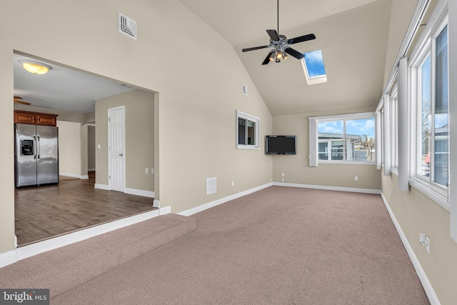 unfurnished living room with a skylight, ceiling fan, carpet floors, and high vaulted ceiling