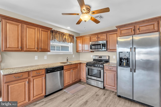 kitchen featuring sink, light hardwood / wood-style flooring, ceiling fan, appliances with stainless steel finishes, and light stone counters