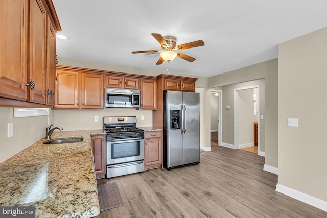 kitchen with appliances with stainless steel finishes, light stone counters, ceiling fan, sink, and light hardwood / wood-style floors