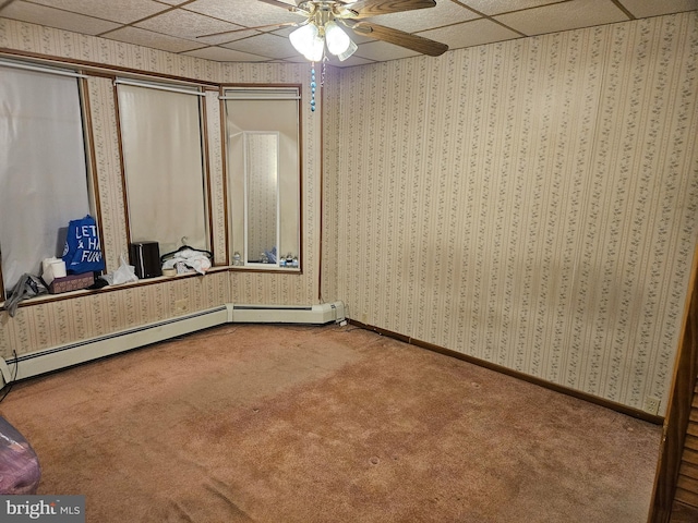 unfurnished bedroom featuring a drop ceiling, baseboard heating, ceiling fan, and carpet flooring