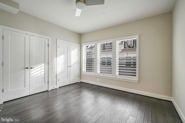 unfurnished bedroom featuring ceiling fan, dark wood-type flooring, and two closets