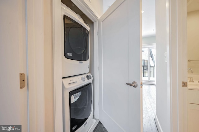 clothes washing area featuring wood-type flooring and stacked washer / dryer