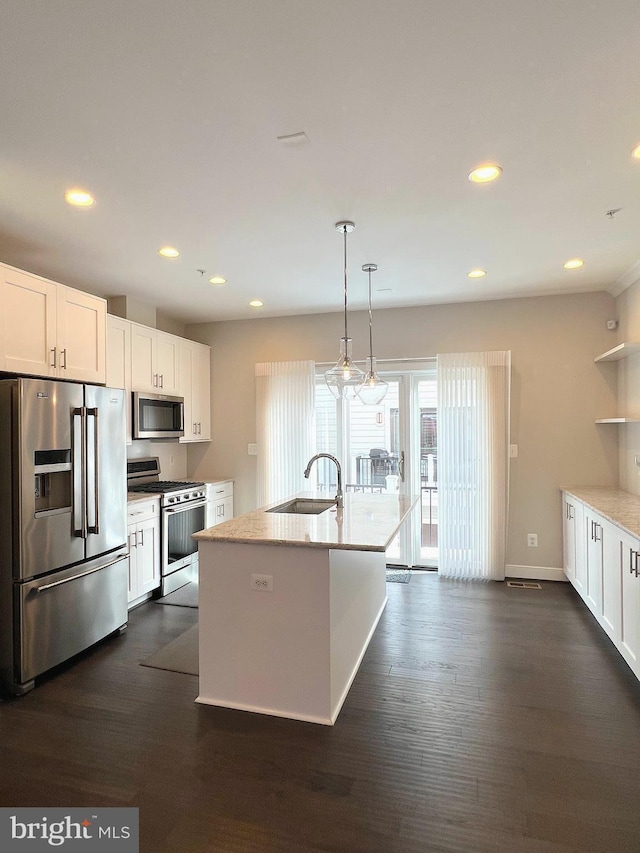 kitchen with appliances with stainless steel finishes, a kitchen island with sink, sink, white cabinets, and hanging light fixtures