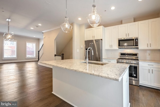 kitchen with pendant lighting, a kitchen island with sink, white cabinets, appliances with stainless steel finishes, and light stone counters