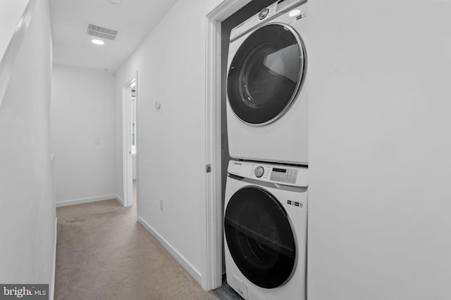 laundry room featuring light carpet and stacked washer / drying machine