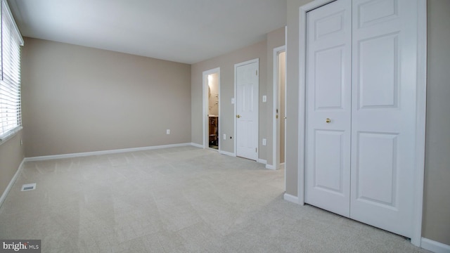 unfurnished bedroom with baseboards, light carpet, a closet, and ensuite bath