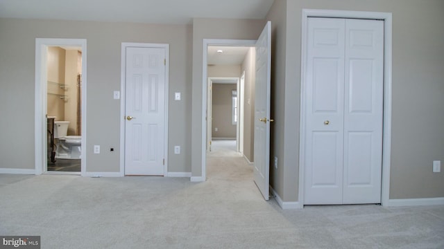 unfurnished bedroom with connected bathroom, baseboards, and light colored carpet