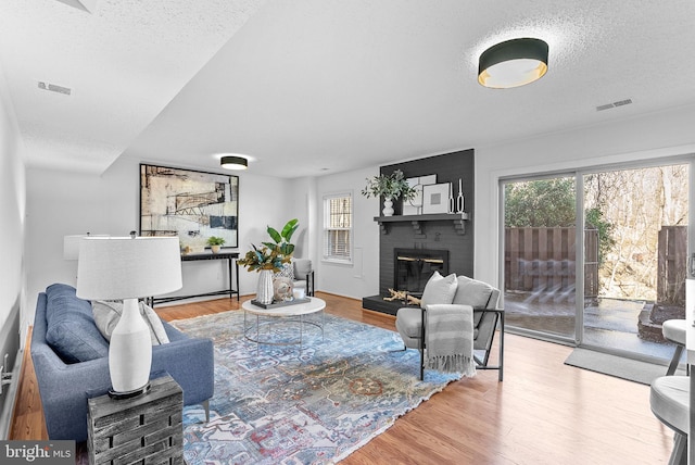 living room featuring a healthy amount of sunlight, a textured ceiling, a brick fireplace, and light wood-type flooring