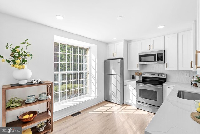 kitchen with sink, white cabinetry, light stone counters, stainless steel appliances, and decorative backsplash