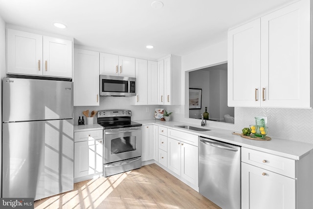 kitchen featuring sink, backsplash, stainless steel appliances, white cabinets, and light wood-type flooring