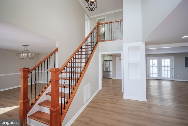 stairs featuring hardwood / wood-style flooring, french doors, ornamental molding, and a notable chandelier