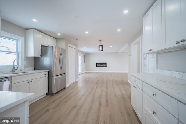 kitchen featuring appliances with stainless steel finishes, light stone counters, sink, light hardwood / wood-style flooring, and white cabinetry