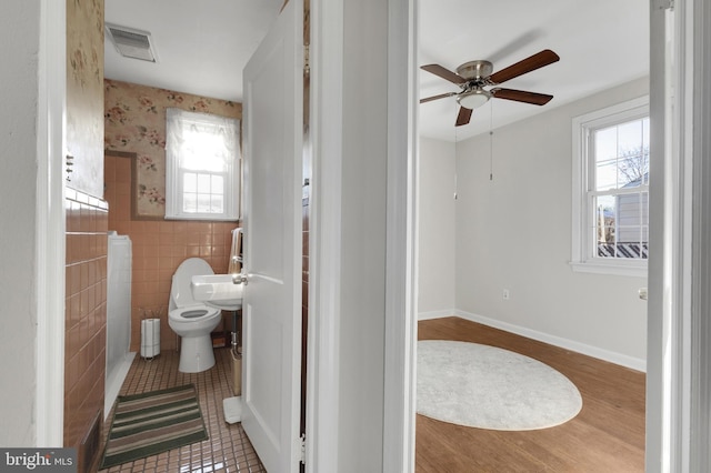 bathroom featuring toilet, ceiling fan, tile walls, and plenty of natural light