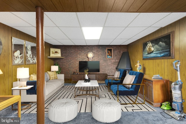 living room with a paneled ceiling, carpet flooring, wood walls, and brick wall