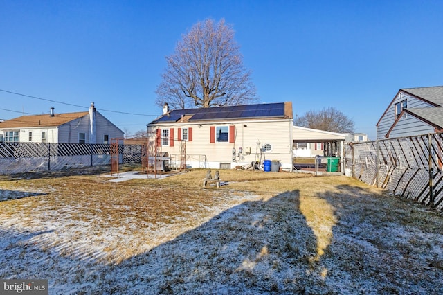 rear view of house featuring roof mounted solar panels, a chimney, and a fenced backyard